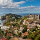 Cliffside condos and villas overlooking a calm Pacific bay in Guanacaste, Costa Rica, with rocky coastline and islands offshore.