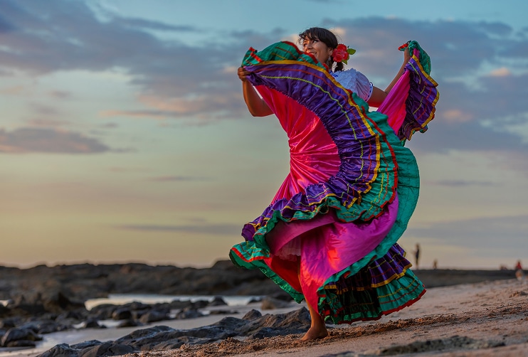 Costa Rican woman performing traditional dance on the beach at sunset, celebrating local culture near areas where U.S. citizens often purchase homes with Costa Rica home loans